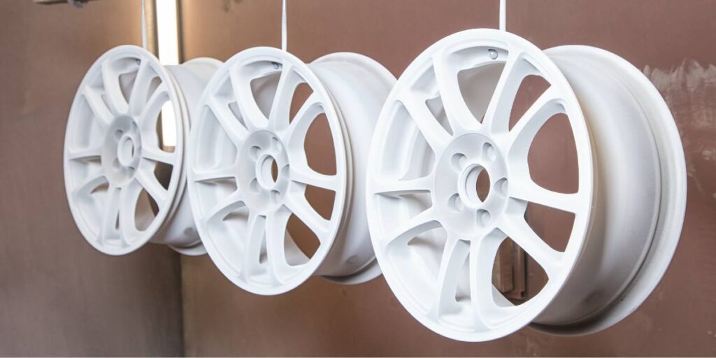 Freshly powder-coated white automotive wheels hanging in a workshop.